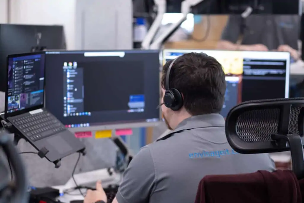 Over the shoulder angle of an Envisage Technology technician working across multiple monitors with Voip headset on