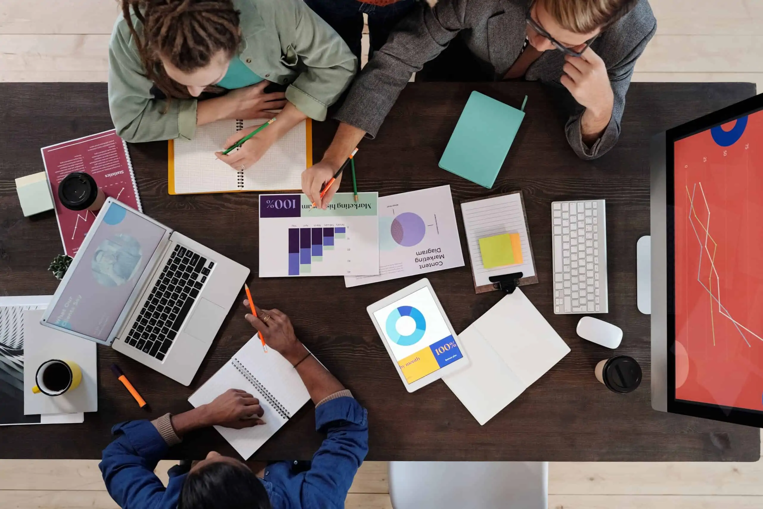 Information Technology How to avoid the most common cause of project failure is represented by a photograph looking down on a desk with three people analysing data and making notes.