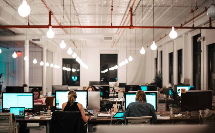How to keep your identity safe online. A photography of a large open workspace with people sitting at their desks in front of computer monitors.