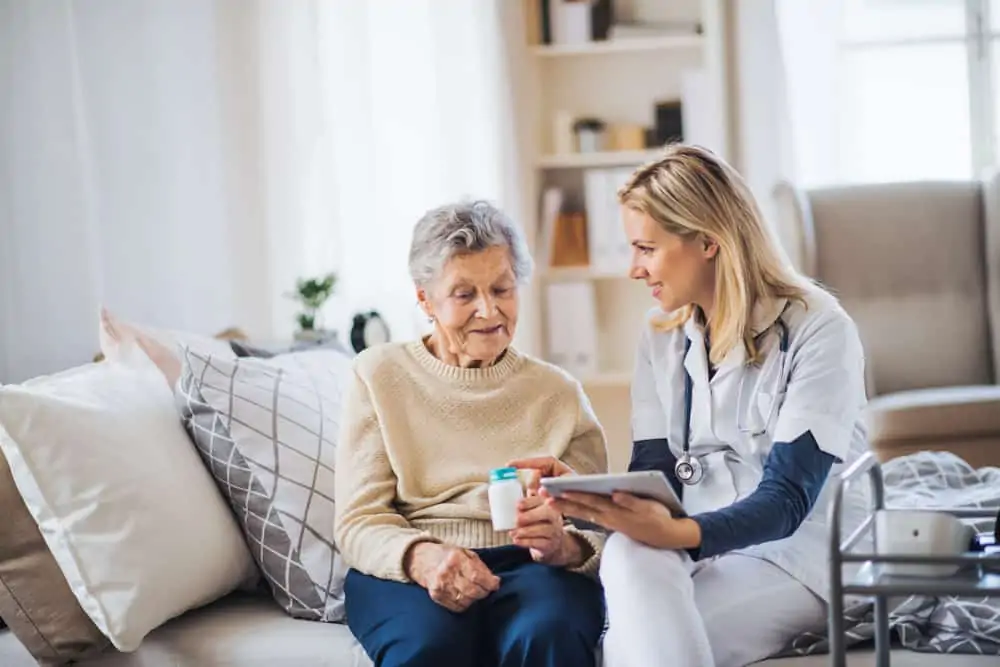 A health visitor with a tablet device explaining medication to a senior woman