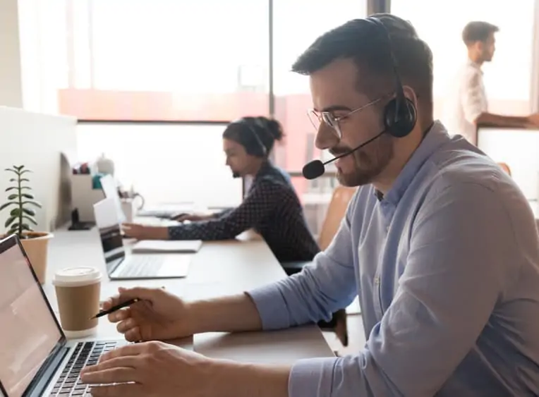 A professional call centre worker wearing a headset and glasses looking at a laptop