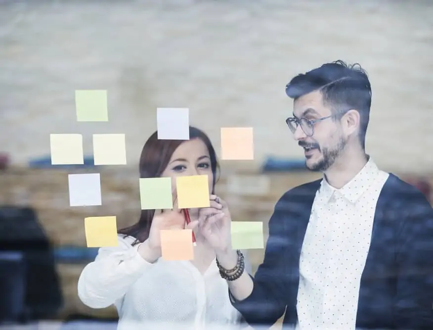 Two employees discussing projects on sticky notes